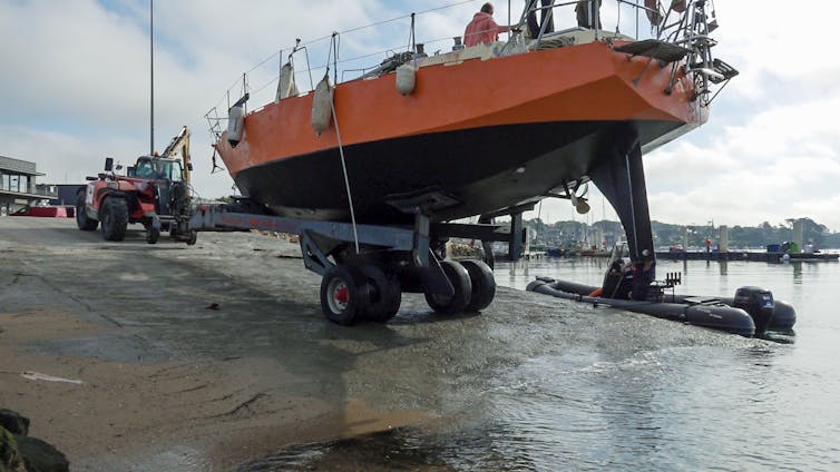 A red and black boat, on a trailer, is being launched into the water